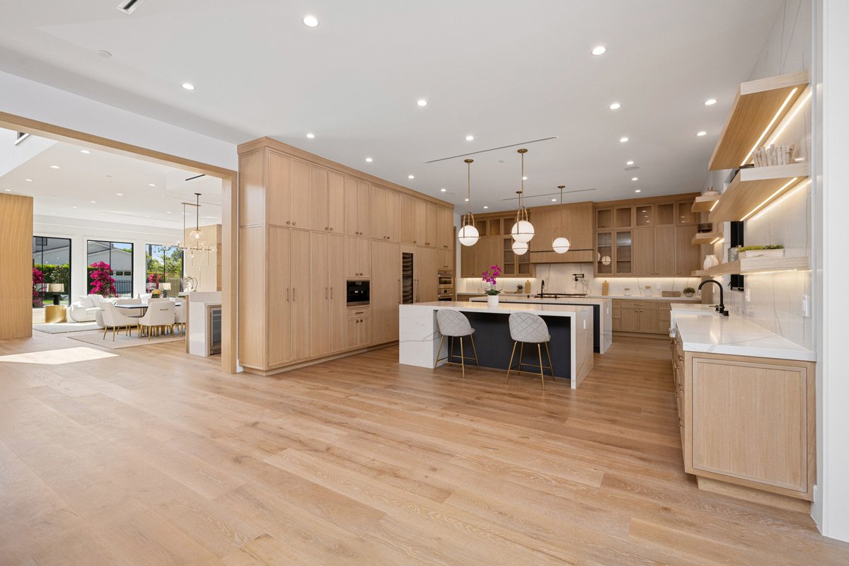 Bright open concept custom kitchen with light white oak cabinetry, a marble waterfall island, gold pendant lights, and glass doors opening to an outdoor area.