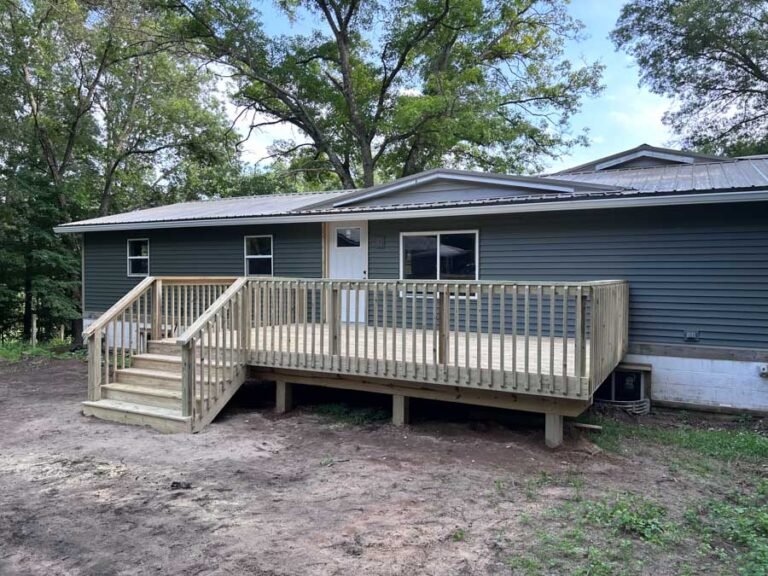 Custom Back Deck Builder in North Shores, Michigan Wide-angle view of a new pressure-treated lumber deck featuring a spacious platform, staircase leading to the yard, and vertical baluster railings.