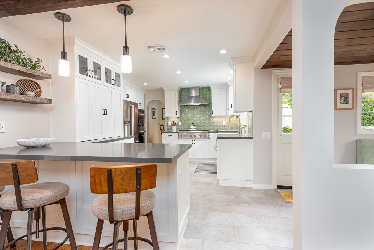 Modern Farmhouse Kitchen with Green Tile Backsplash | Design Ideas A beautiful kitchen featuring white shaker cabinets, a large island with a dark countertop and wood-back bar stools, open shelving, and a striking green tile backsplash behind the stainless steel range.
