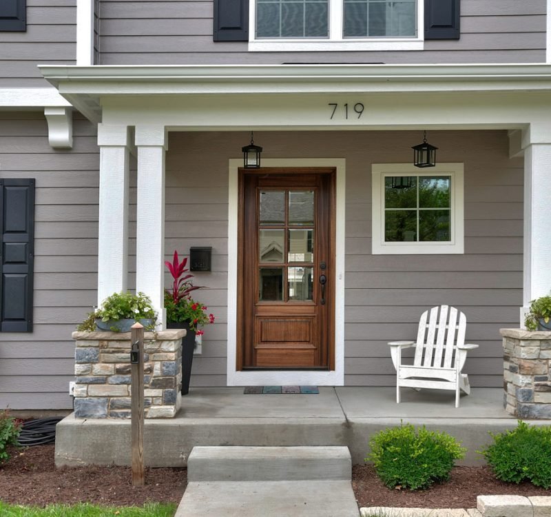Beautiful Home Exterior with Stone Pillar Porch | Hutch Homes A charming home exterior showcasing a covered front porch with white columns on stacked stone pillars, a custom wood front door, and professional landscaping.